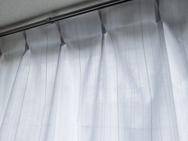 自然光が溢れる室内の様子を演出する、白いレースのカーテンがかかった窓。