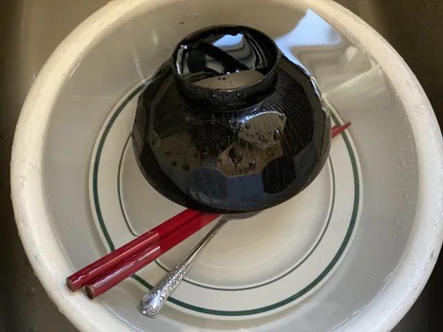 水が溜まった洗い桶の中に、黒いお椀と赤い箸が入っている様子が映っています。