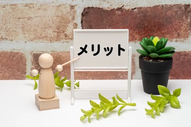 「メリット」と書かれたホワイトボードを指し示している人形と、緑の植物が置かれた写真